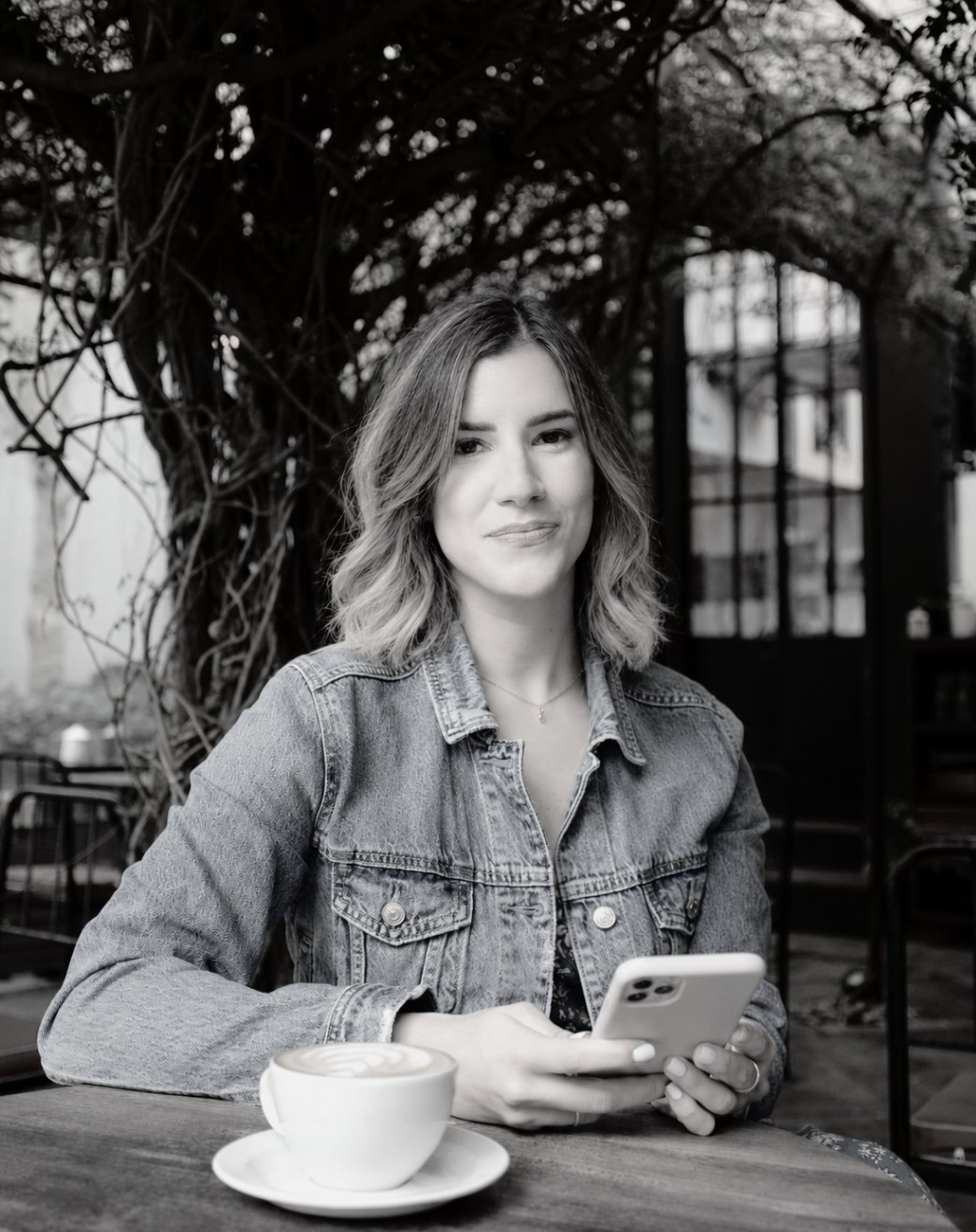 Veronica at a café table with a latte and her phone, black and white portrait