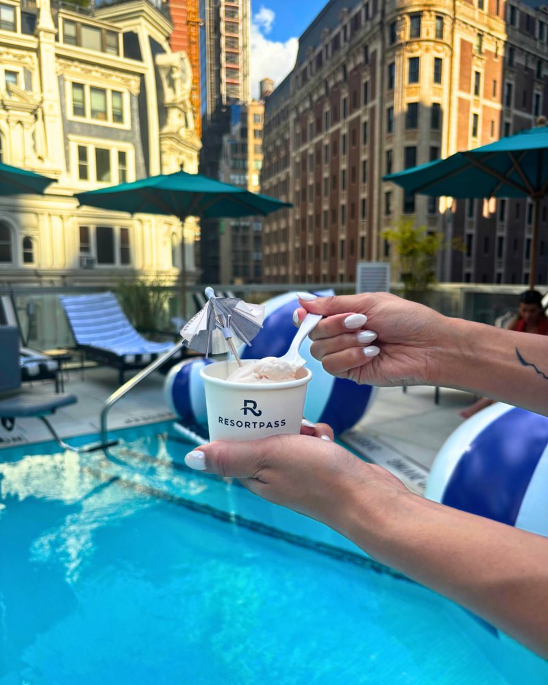 A ResortPass ice cream cup held over a rooftop pool